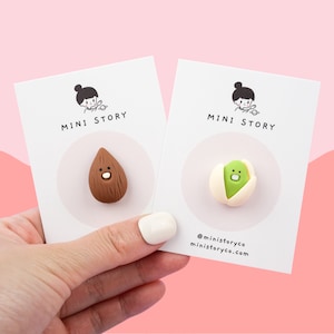 May include: Two cards with the text "MINI STORY" on them. The card on the left has a brown almond with a face on it. The card on the right has a green pistachio with a face on it.