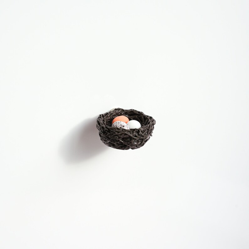 May include: A small brown woven bird's nest with three speckled eggs inside. Two of the eggs are white and one is light pink.