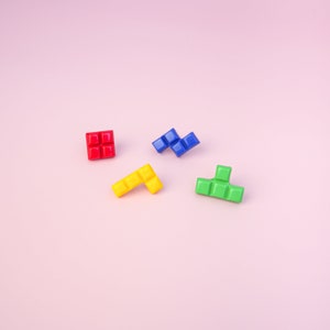 May include: Four colorful plastic Tetris blocks on a pink background. The blocks are red, blue, yellow, and green.