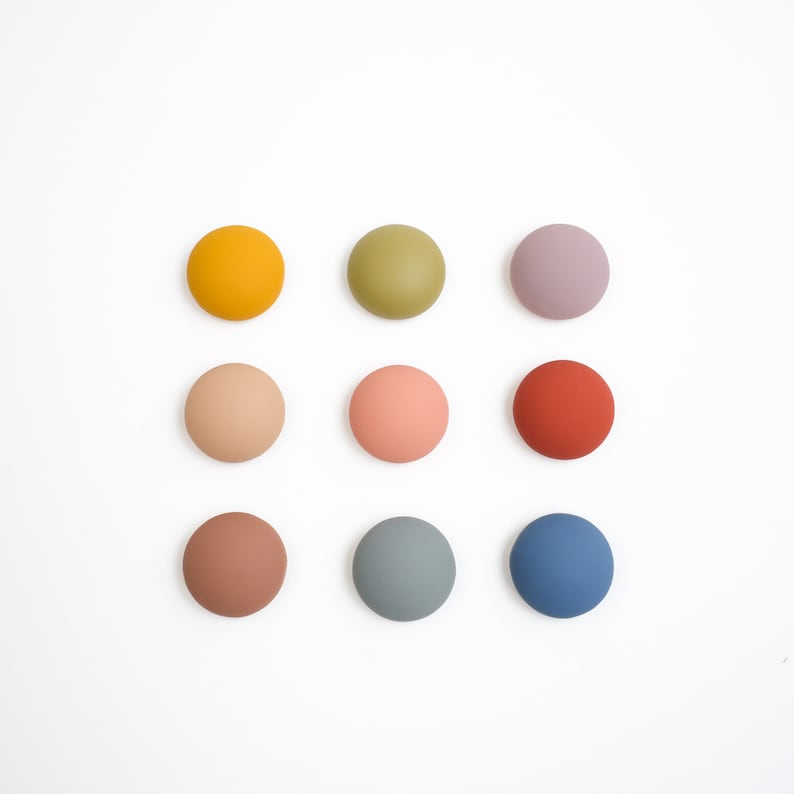 Pu&ograve; includere: Nove dischi rotondi in legno dipinti di colori vivaci. I dischi sono disposti in una griglia 3x3. I colori sono giallo, verde, viola, beige, rosa, rosso, marrone, blu e blu chiaro.