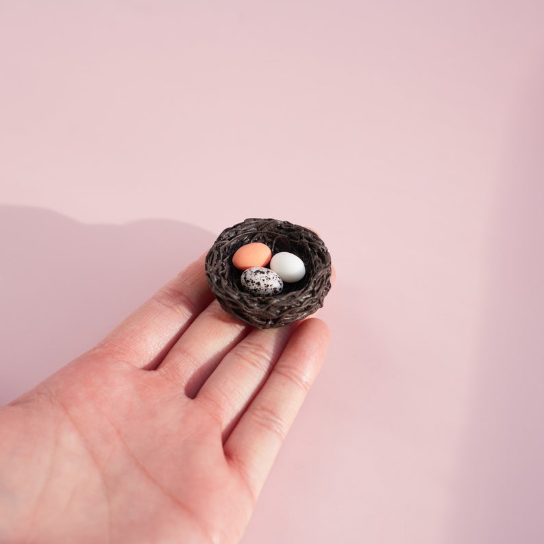 May include: A small brown woven bird's nest with three eggs inside. The eggs are white, speckled brown, and light pink.