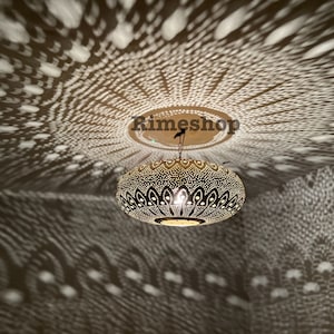 Puede incluir: Una lámpara de techo redonda de metal negro con intrincados diseños recortados. La luz proyecta una sombra con patrones en el techo, creando un efecto decorativo.