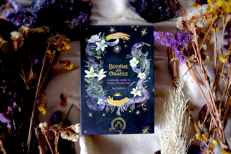 May include: A black book with a gold title "Become an Oracle: A Magical Guide to Divine Connection" with a snake and flowers illustration on the cover.