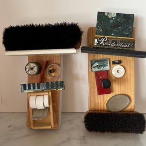 May include: Two abstract wooden sculptures resembling faces. One has a black brush for hair, a spool of thread for an eye, and a computer chip for a mouth. The other has a black brush, a green marble piece, and the word "Presidential".