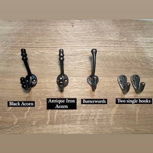 Pu&ograve; includere: Quattro diversi stili di ganci in metallo nero montati su una superficie in legno. I ganci sono etichettati "Black Acorn", "Antique Iron Acorn", "Butterworth" e "Two single hooks".