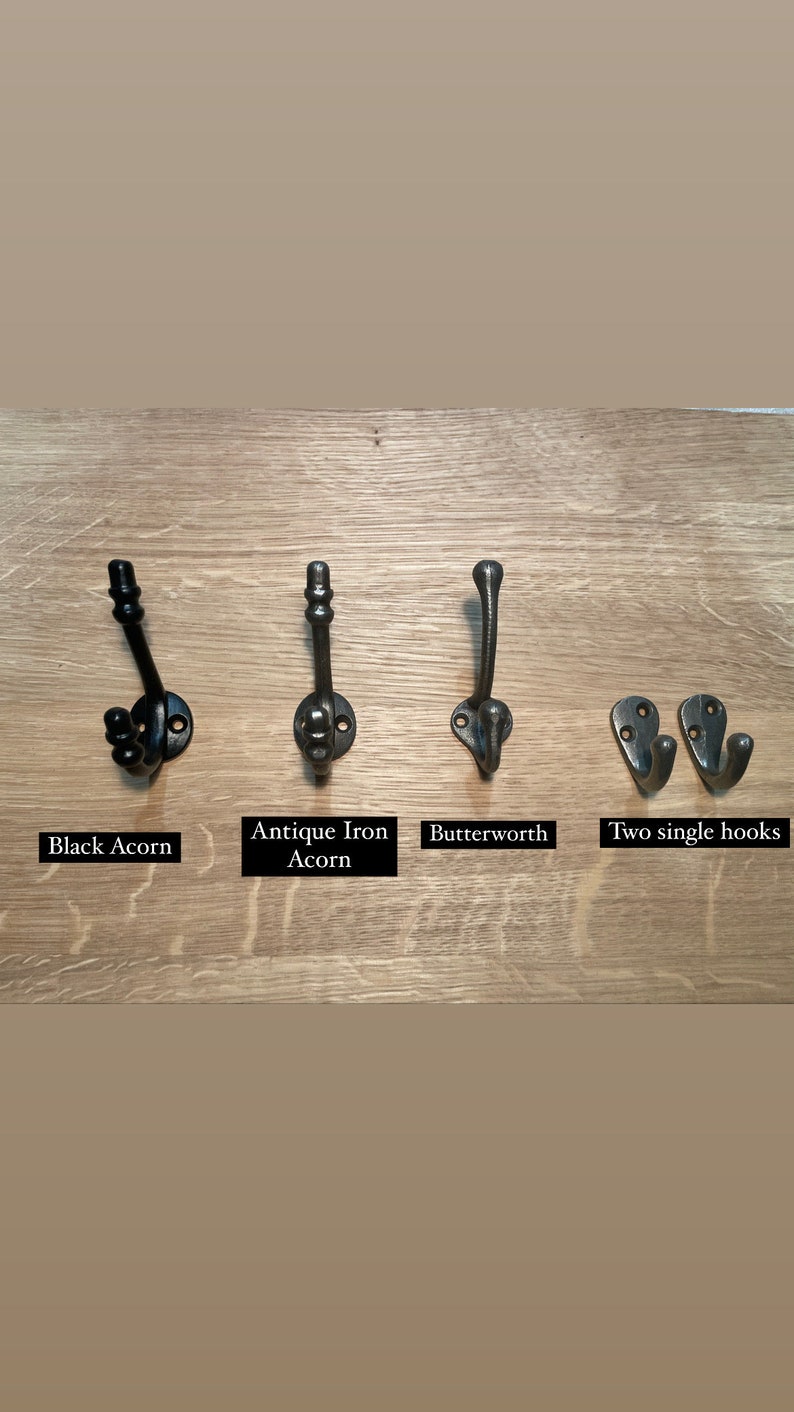 Pu&ograve; includere: Quattro diversi stili di ganci in metallo nero montati su una superficie in legno. I ganci sono etichettati "Black Acorn", "Antique Iron Acorn", "Butterworth" e "Two single hooks".