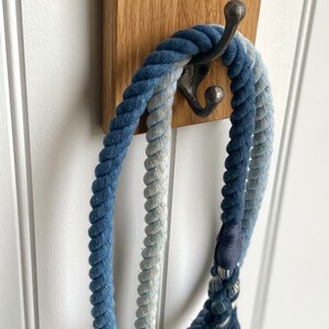 May include: A wooden wall hook with the word "WALKIES" engraved on it. A blue and white rope dog leash is hanging on the hook.