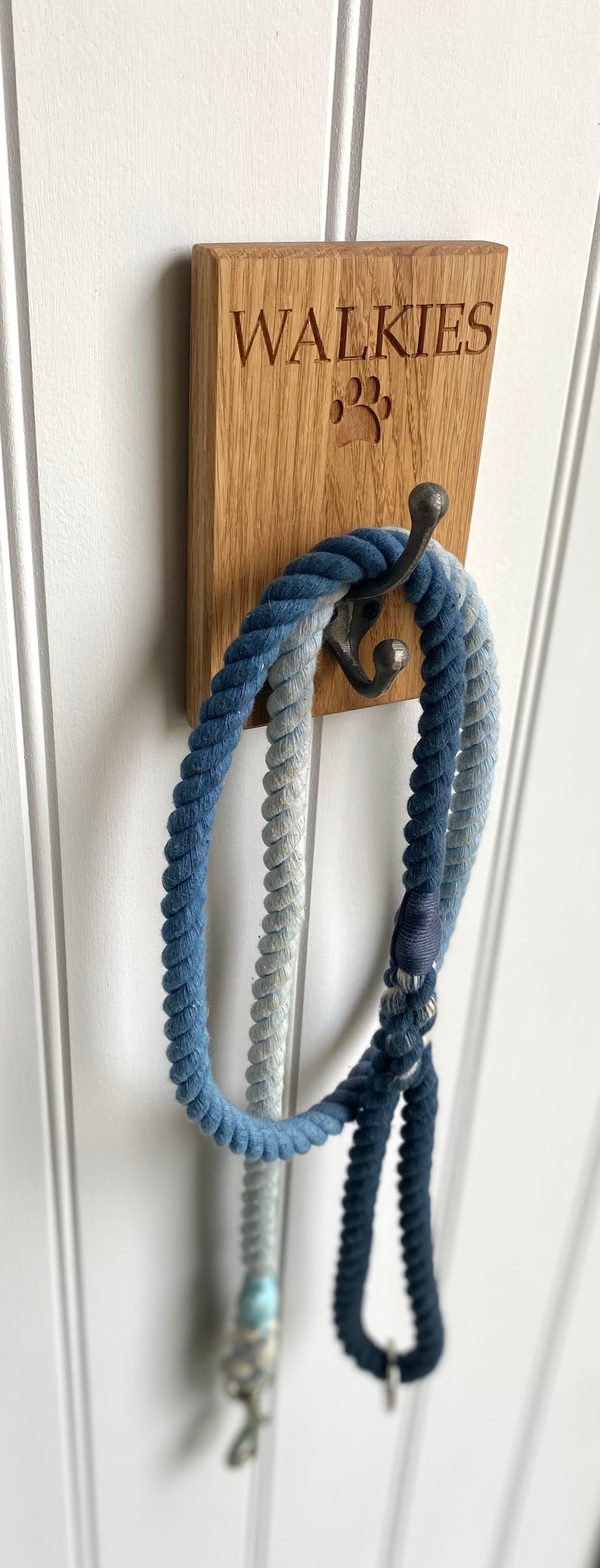May include: A wooden wall hook with the word "WALKIES" engraved on it. A blue and white rope dog leash is hanging on the hook.