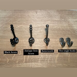 May include: Four different styles of black metal hooks mounted on a wooden surface. The hooks are labeled "Black Acorn", "Antique Iron Acorn", "Butterworth", and "Two single hooks".