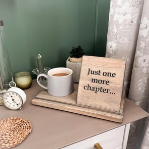 May include: A bedside table arrangement with a grey mug of coffee, a wooden sign saying "Just one more chapter...", and a small succulent plant. A white alarm clock and a woven coaster are also present, creating a relaxing atmosphere.