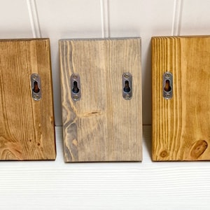 Pu&ograve; includere: Tre mensole a muro in legno con due fori ciascuna. Le mensole sono tinte in tre colori diversi: legno naturale, grigio e marrone scuro.