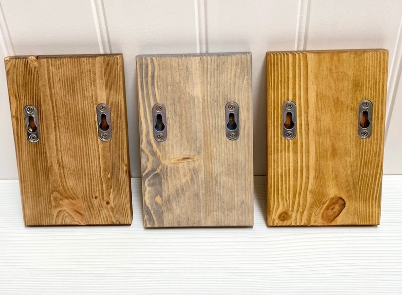 Pu&ograve; includere: Tre mensole a muro in legno con due fori ciascuna. Le mensole sono tinte in tre colori diversi: legno naturale, grigio e marrone scuro.
