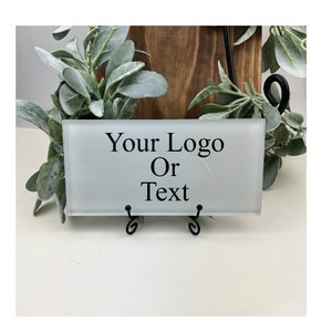 May include: White frosted glass tile with black text that reads "Your Logo Or Text" on a black metal stand.