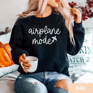 Pu&ograve; includere: Una felpa nera con la scritta "airplane mode" e un piccolo aereo grafico in bianco.