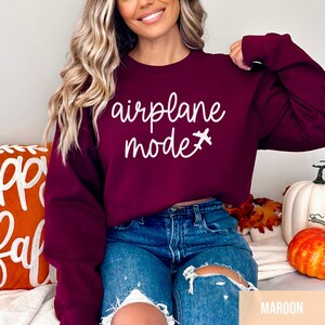 Pu&ograve; includere: Una felpa color granata con la scritta "airplane mode" in lettere bianche e una piccola icona di aereo.