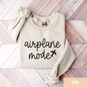 Pu&ograve; includere: Una felpa beige con la scritta "airplane mode" e una piccola icona di aereo stampata in nero.