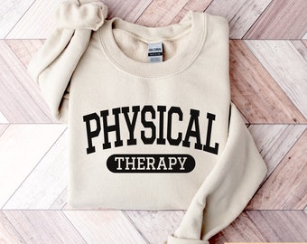 May include: A sand-colored sweatshirt with the text "PHYSICAL THERAPY" in black lettering. The text is in a collegiate font style.
