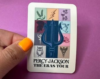May include: A sticker with a blue trident in the center, surrounded by nine squares with different symbols representing the Greek gods. The text "Percy Jackson The Eras Tour" is at the bottom.