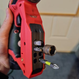 May include: A red and black cordless drill with a built-in bit holder. The holder has a variety of bits, including a 7/16 inch socket.