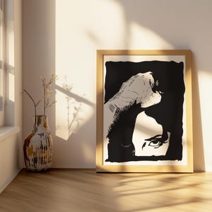 May include: Black and white illustration of a woman's face with a hand covering part of her head. The image is framed in a light wood frame.