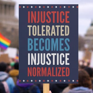 May include: A sign held up at a protest with the words "INJUSTICE TOLERATED BECOMES INJUSTICE NORMALIZED" in red, white, and blue. The sign is held in front of a crowd of people, with a rainbow flag visible in the background.