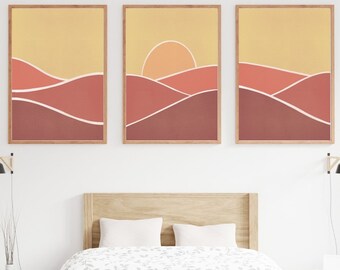 May include: Three abstract landscape prints with a sunset in the middle print. The prints are framed in natural wood and feature a yellow background with red and brown hills.