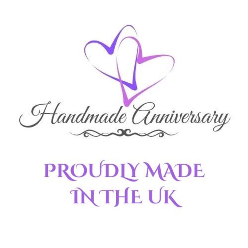Puede incluir: Un logotipo gr&aacute;fico que presenta dos contornos de corazones morados superpuestos en la parte superior. Debajo, el texto Handmade Anniversary aparece en cursiva negra, seguido del texto morado PROUDLY MADE IN THE UK en fuente serif.