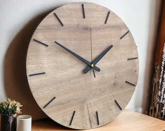 May include: A round wooden wall clock with black hour and minute hands. The clock face has a wood grain pattern and black Roman numeral markings.