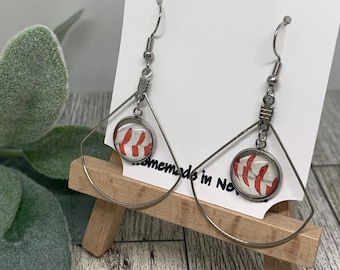Puede incluir: Pendientes de plata en forma de lágrima con un diseño de béisbol. Los pendientes presentan un cabujón de vidrio transparente con un diseño de béisbol rojo y blanco. Los pendientes están hechos a mano en Carolina del Norte.