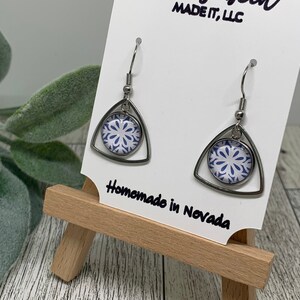 May include: Silver triangle earrings with a blue and white patterned circle in the center. The earrings are on a white card with the text "Molly Beth MADE IT, LLC" and "Homemade in Nevada".