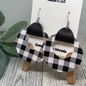 May include: A pair of black and white checked circle earrings with a brown leather accent. The earrings are hanging from silver hooks. The text "Home" and "Nevada" are visible on the earrings.