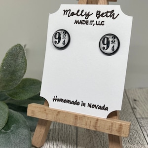 May include: A pair of black and white glass earrings with the number "9 3/4" printed on them. The earrings are displayed on a white card with the text "Molly Beth Made It, LLC" and "Homemade in Nevada".