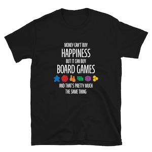 May include: Black t-shirt with white text that reads "Money can't buy happiness but it can buy board games" and a row of colorful game pieces below. The text continues "And that's pretty much the same thing."