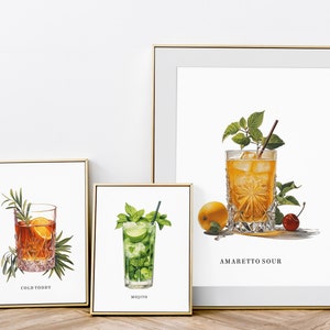 May include: Three framed prints of cocktails. The first print shows a glass of "Cold Toddy" with a sprig of rosemary. The second print shows a glass of "Mojito" with mint leaves. The third print shows a glass of "Amaretto Sour" with a cherry and a lemon wedge.