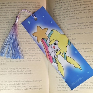 Op de afbeelding: Blauwe boekenlegger met een stripfiguur met een sterrenstaf, tegen een sterrenhemel. De boekenlegger heeft een blauwe kwast en de tekst "Made by Mias".