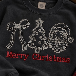 May include: A black crewneck sweatshirt featuring embroidered line art of a bow, a Christmas tree, and Santa Claus. Below the embroidery, the text Merry Christmas is stitched in red thread. The inner collar tag reads Comfort Colors.