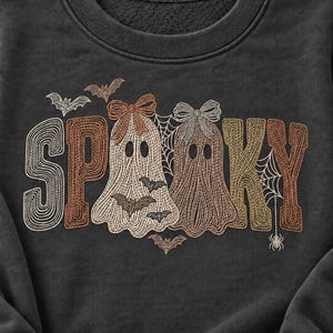 May include: A dark charcoal gray crewneck sweatshirt featuring an embroidered design that spells out SPOOKY. The letters are integrated with two ghosts wearing bows, small flying bats, spiderwebs, and a spider in shades of cream, tan, and brown.