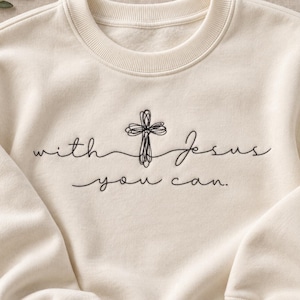 May include: A cream-colored crewneck sweatshirt featuring black embroidered text that reads "with Jesus" and "you can." with a central embroidered cross design made of continuous looping lines centered on the chest.