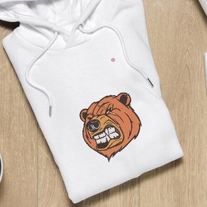 May include: White hooded sweatshirt with a brown bear face graphic. The bear has a fierce expression with sharp teeth and a furrowed brow.