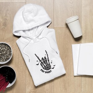 May include: White hooded sweatshirt with a black skeleton hand graphic and the text "Stay Spooky".