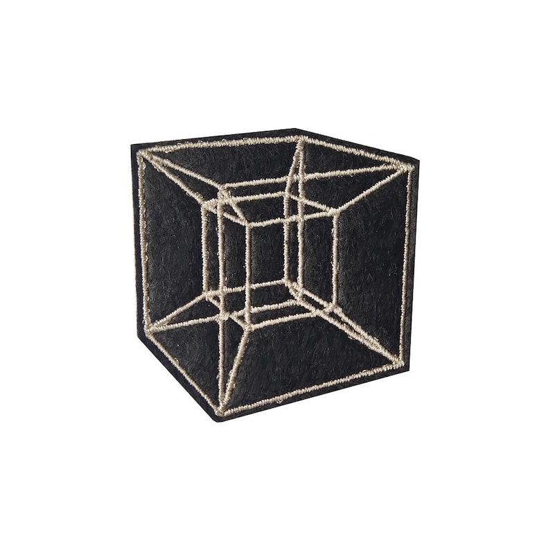 May include: A black square patch featuring a three-dimensional geometric cube design in a light beige color. The cube's lines are stitched onto the patch, creating a textured effect. The patch is likely for clothing or accessories.