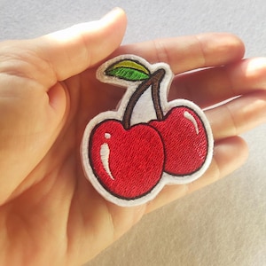 Pode incluir: Remendo de cereja bordado com duas cerejas vermelhas brilhantes com destaques brancos e um caule marrom. O remendo tem uma borda branca e uma folha verde e amarela. Ideal para adicionar a roupas ou acessórios.