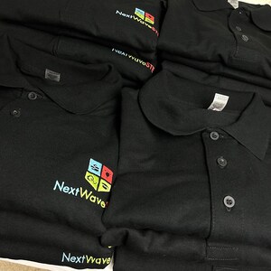 May include: A stack of black polo shirts with a colorful logo that says "NextWave" on the left chest.