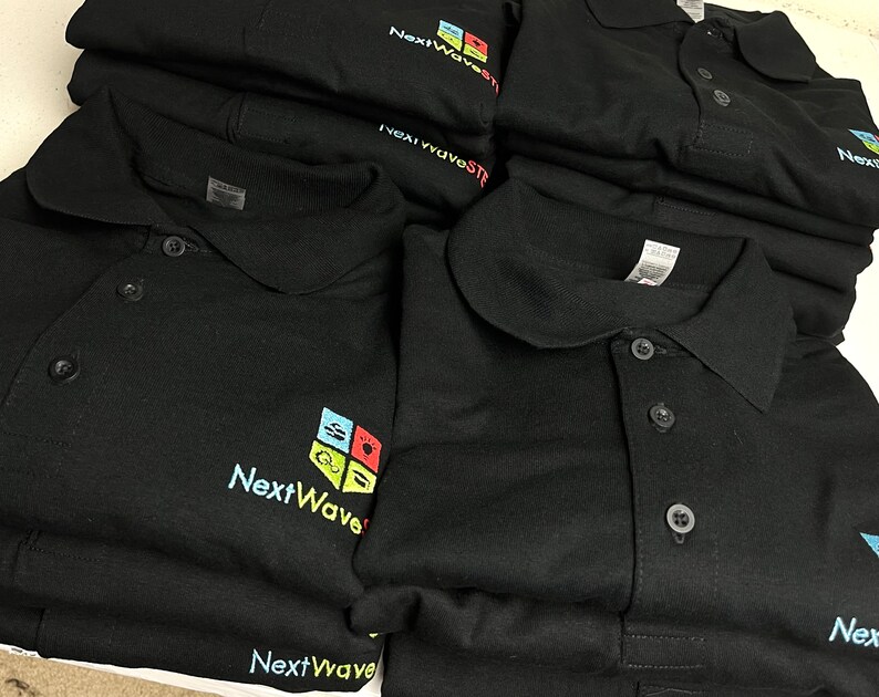 May include: A stack of black polo shirts with a colorful logo that says "NextWave" on the left chest.
