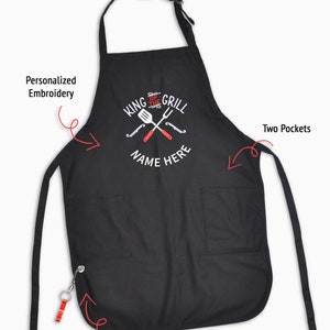 Pode incluir: Avental preto com o texto "KING OF THE GRILL NAME HERE" e um gr&aacute;fico de utens&iacute;lios de churrasco. Possui dois bolsos, uma al&ccedil;a de pesco&ccedil;o de 2,5 cm de largura, bordado personalizado e um abridor de garrafas remov&iacute;vel.