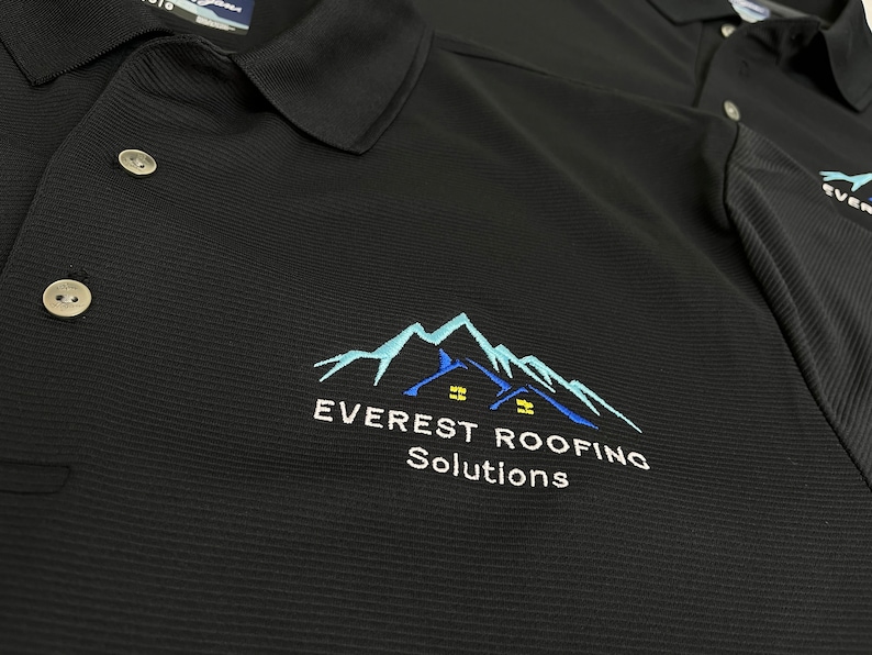 May include: Black polo shirt with a white embroidered logo that says "EVEREST ROOFING Solutions" and features a blue mountain range with two houses.
