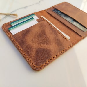 May include: A brown leather wallet with a stitched edge and multiple card slots. The wallet is open and has cards inside.