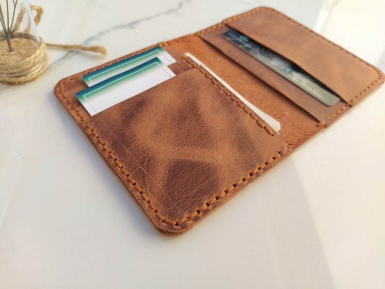 May include: A brown leather wallet with a stitched edge and multiple card slots. The wallet is open and has cards inside.