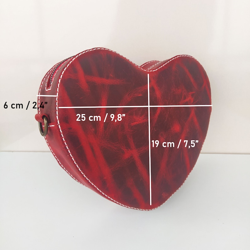 May include: Red leather heart-shaped handbag with white stitching. The bag measures 9.8 inches wide, 7.5 inches tall, and 2.4 inches deep.