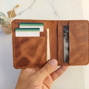 May include: A brown leather wallet with a stitched edge, open to reveal two card slots and a larger pocket for bills. The wallet has a worn, distressed look.